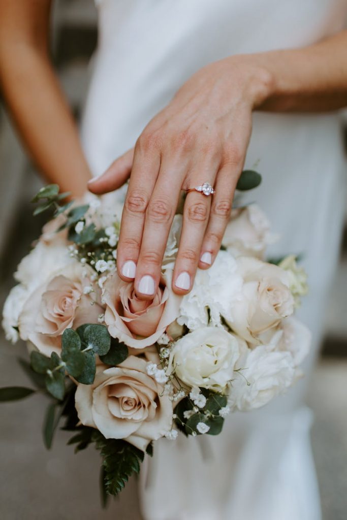 Close-up of a bridal bouquet and manicured hand showcasing an elegant engagement ring.